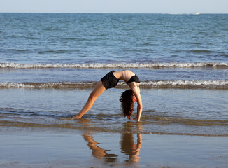 girl performs gymnastic exercises arching her back and forming a heart in the reflection on the water