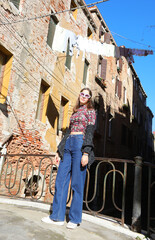 girl with mask wearing blue jeans trousers posing near houses with clothes hanging out to dry in the sun in Venice in Italy