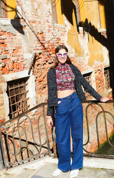 smiling girl with venetian mask wearing blue jeans trousers posing near houses with clothes hanging out to dry in the sun in Venice in Italy
