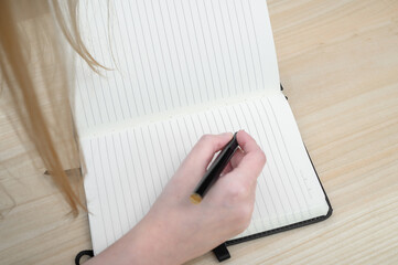 Kobieta zapisuje coś w zeszycie w linie, pochylona nad stolikiem - obrazy, fototapety, plakaty