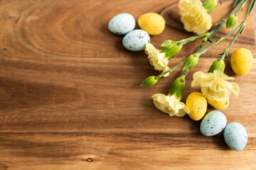 Fototapeta na wymiar Yellow flowers and pastel yellow and blue colored eggs on a background of brown wood. Layout. Mockups. Springs background. Easter background. Easter eggs close up