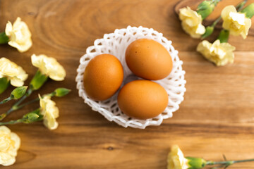 Yellow flowers and brown organic eggs in a white small wicker basket on a background of brown wood. Layout. Mockups. Pastel Springs background. Easter background. Easter eggs close up