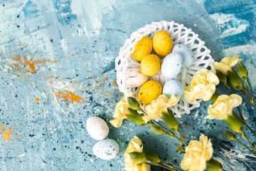Yellow beautiful flowers and blue, yellow colored easter eggs in wicker basket on a blue picturesque oil painting background close up. spring Mockups. Layout. Easter pastel contemporary background