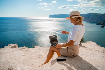 Freelance women sea working on the computer. Good looking middle aged woman typing on a laptop keyboard outdoors with a beautiful sea view. The concept of remote work.