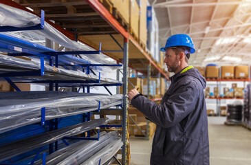 Young caucasian man in helmet, worker in warehouse checking pipe goods. Stock of Parcels with Products, transportation concept