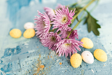Pink flowers and yellow and white colored easter eggs on a blue picturesque oil painting background...