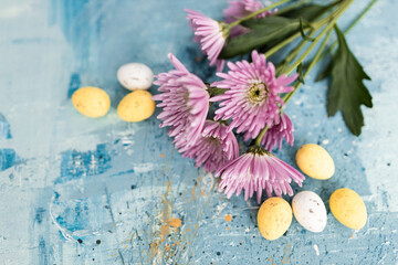 Pink flowers and yellow and white colored easter eggs on a blue picturesque oil painting background close up. Spring Mockups with pink Gerbers. Layout. Easter pastel background