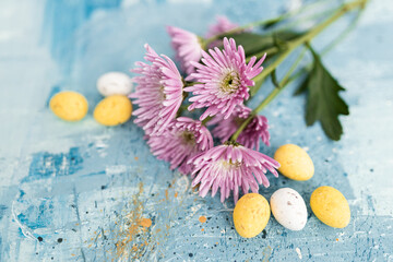 Obraz na płótnie Canvas Pink flowers and yellow and white colored easter eggs on a blue picturesque oil painting background close up. Spring Mockups with pink Gerbers. Layout. Easter pastel background
