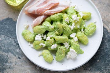 Potato gnocchi served with green pea sauce, feta and bacon on a white plate, horizontal shot on a...