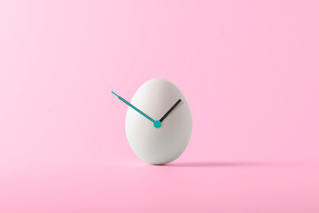 Creative Easter concept. White Easter egg with hour hands on pink background. Easter time.