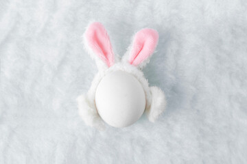 Creative Easter concept. White egg with fluffy ears of Easter bunny on fluffy soft white background...