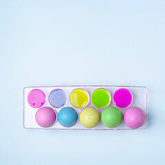 Multicolored easter eggs in egg tray with multicolored pastel colors on blue background. Creative Easter concept.