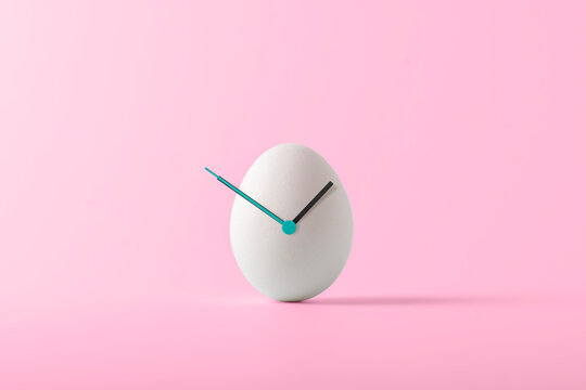 Creative Easter concept. White Easter egg with hour hands on pink background. Easter time.