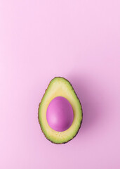 Creative Easter concept. Cut avocado with pink easter egg on pink background with copy space.