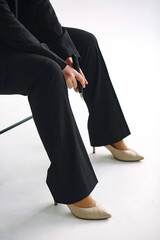 Close up photo of woman in black suit and beige heels sitting on the stool and holding a permanent makeup machine. Space for text