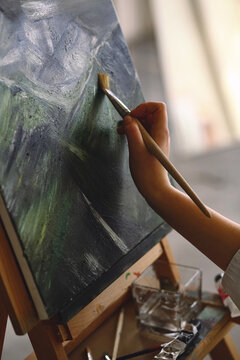 Female artist hand holding a brush in her hand and draws a painting. The artistic process. Close up photo