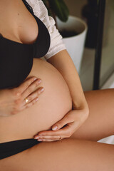 Pregnant woman in black underwear touching her belly. Close up photo of pregnant belly