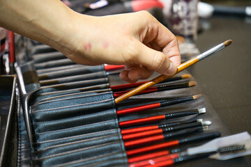Hand reaching for row of make-up brush in leather brush roll.
