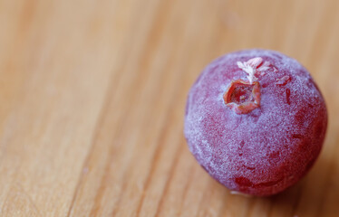 One frosted cranberry on wooden surface, close-up, macro