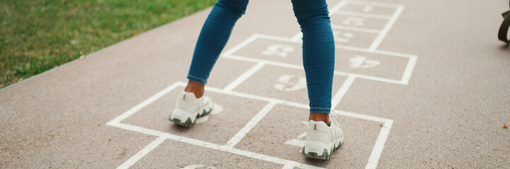 Close-up of young woman hopscotching on city playground, Panorama. Closeup of the legs of girl...