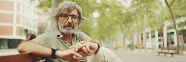 Panorama of thoughtful middle-aged man with gray hair and beard wearing casual clothes sits on...