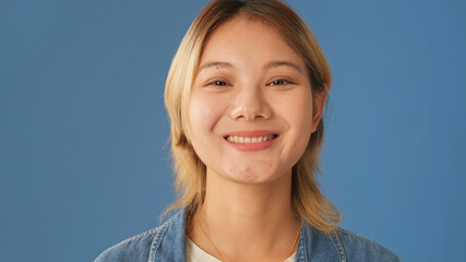 Close-up, smiling woman looks at camera isolated on blue background in studio