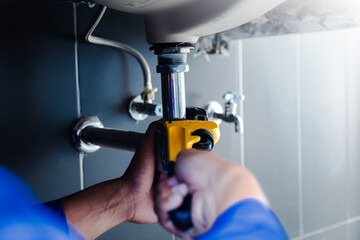 Plumber fixing white sink pipe with adjustable wrench.