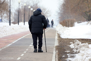 Elderly man with walking cane on a winter street. Concept of limping, old age, snow weather