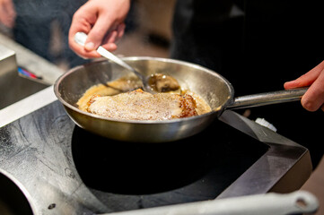 A close-up of hands cooking meat in a sizzling pan. The meat sears as bubbles form, set against a modern kitchen backdrop.