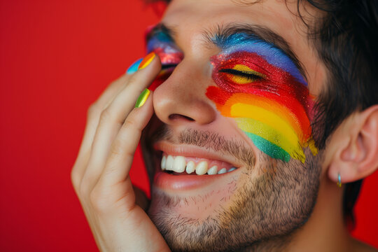A man with rainbow face paint is smiling and making a funny face