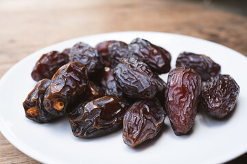 Brown dried Medjool dates in a white plate are sweet and juicy. They are eaten by Muslims during fasting.