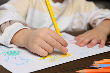 Little boy drawing with pencil at wooden table, closeup. Child`s art