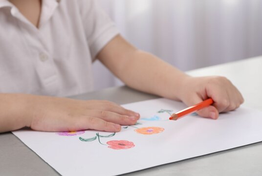 Little boy drawing flowers with pencil at grey table indoors, closeup. Child`s art