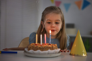 Cute girl with birthday cake at table indoors