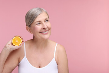 Beautiful woman with half of orange rich in vitamin C on pink background, space for text