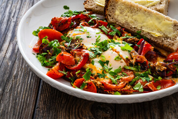 Shakshuka - fried eggs with vegetables on wooden table

