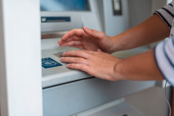 A woman enters a pin code at an ATM. The woman hides her pin with her hand closeup - obrazy, fototapety, plakaty