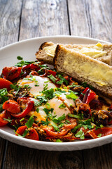 Shakshuka - fried eggs with vegetables on wooden table
