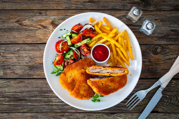 Crispy breaded fried pork loin chops with fries and fresh vegetables on wooden table
