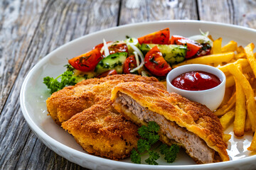 Crispy breaded fried pork loin chops with fries and fresh vegetables on wooden table

