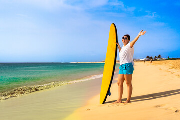 Beautiful woman holding surfboard standing on sunny beach Santa Maria, Sal island , Cape Verde
