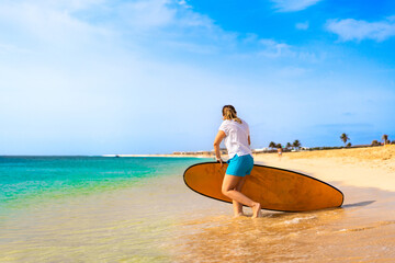 Naklejka na ściany i meble Beautiful woman holding surfboard standing on sunny beach Santa Maria, Sal island , Cape Verde 