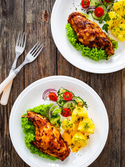 Cooked rabbit thighs with potatoes and fresh vegetable salad on wooden table
