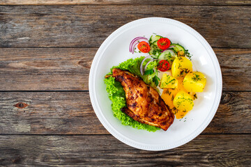 Cooked rabbit thighs with potatoes and fresh vegetable salad on wooden table
