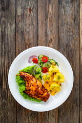 Cooked rabbit thighs with potatoes and fresh vegetable salad on wooden table
