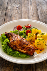 Cooked rabbit thighs with potatoes and fresh vegetable salad on wooden table
