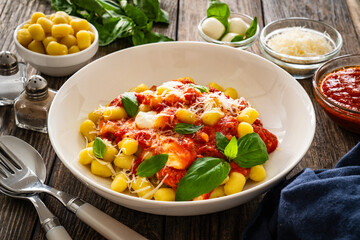Gnocchi alla sorrentina - gnocchi with melted mozzarella cheese in tomato sauce and Parmigiano Reggiano on wooden table
