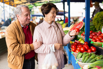 Elderly man and a woman buy tomatoes at an open air market