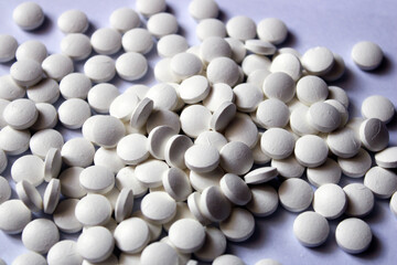 Fototapeta na wymiar A lot of white pills are scattered on a white background.