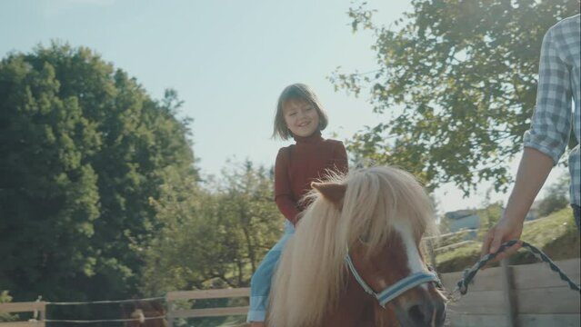Young girl riding brown pony on a small pony ranch in the countryside. Fun family acitivity on a sunny day. Equestrian animals. 